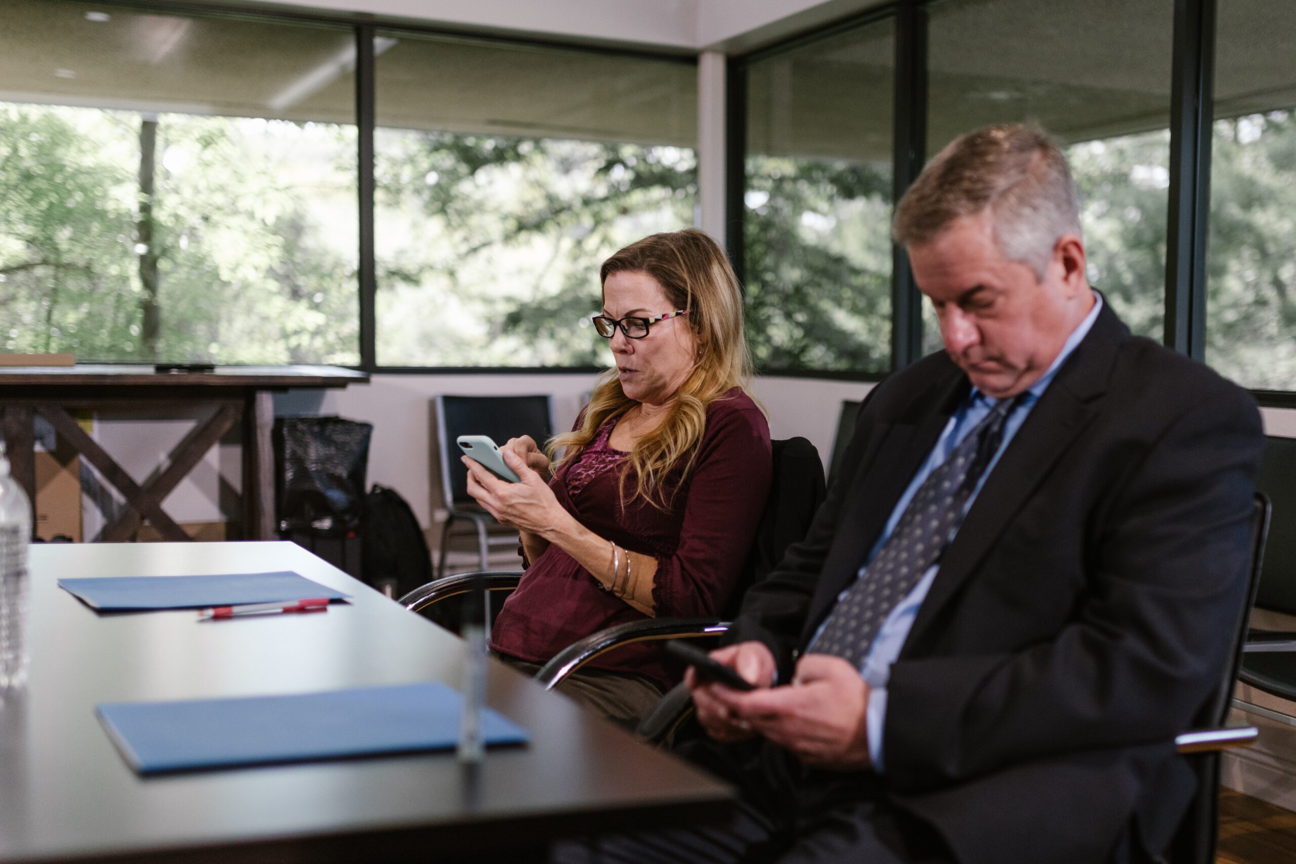 Dwoje ludzi z rady nadzorczej w firmie siedzący przy stole i bawiący się telefonami komórkowymi