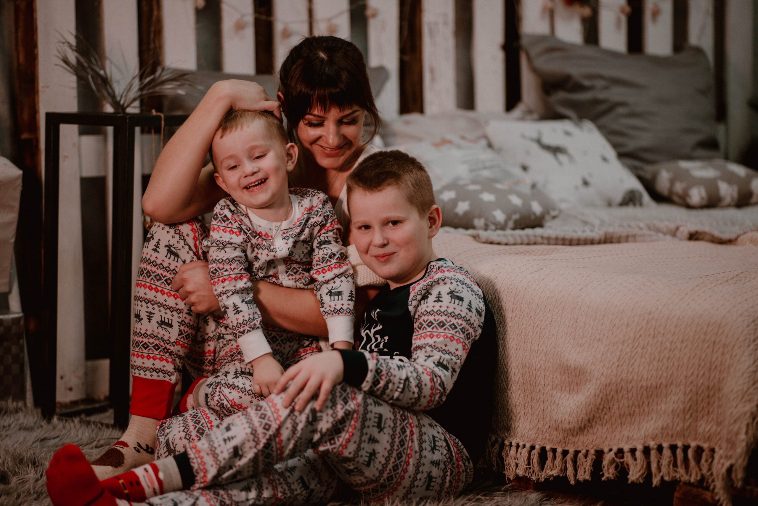 Kobieta z dwoma synami ubrani w piżamy siedzący przed łóżkiem w sypialni